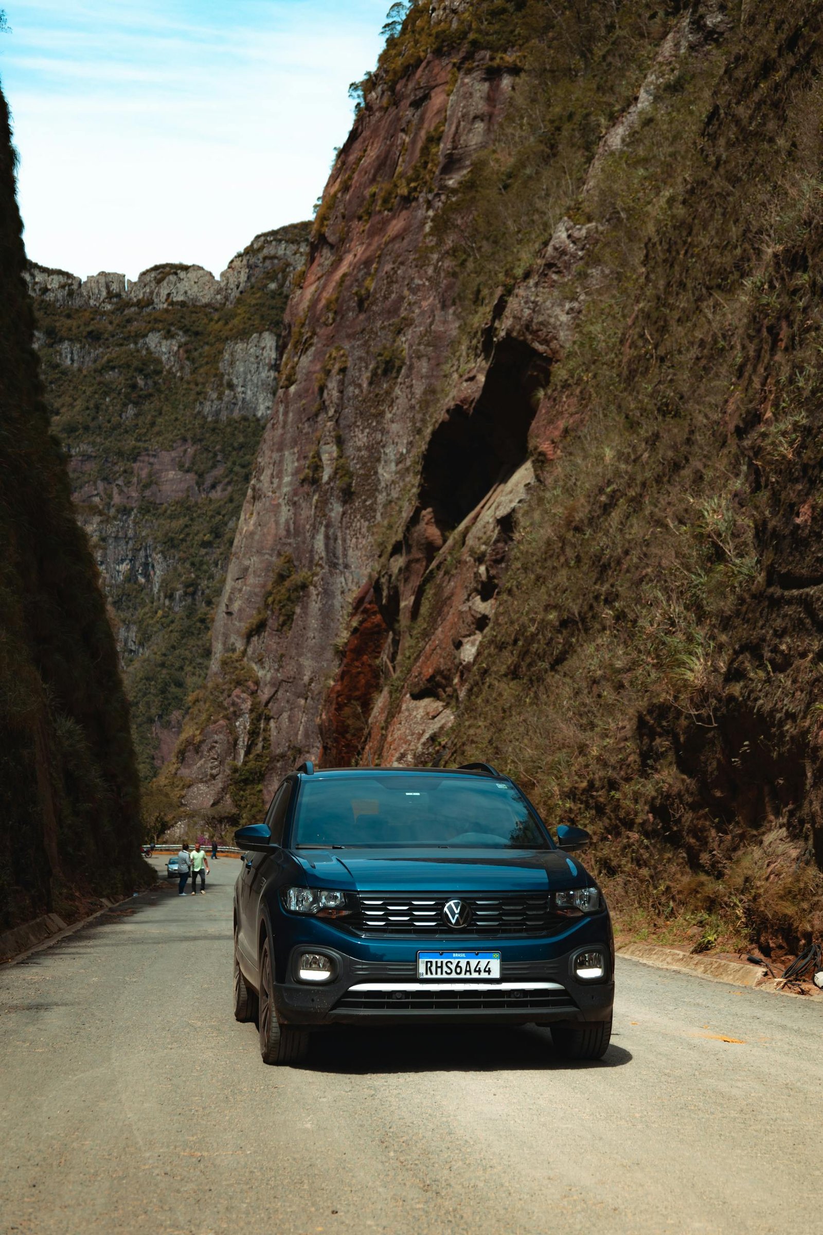 Black SUV driving along a road flanked by towering cliffs in a rural mountain setting.
